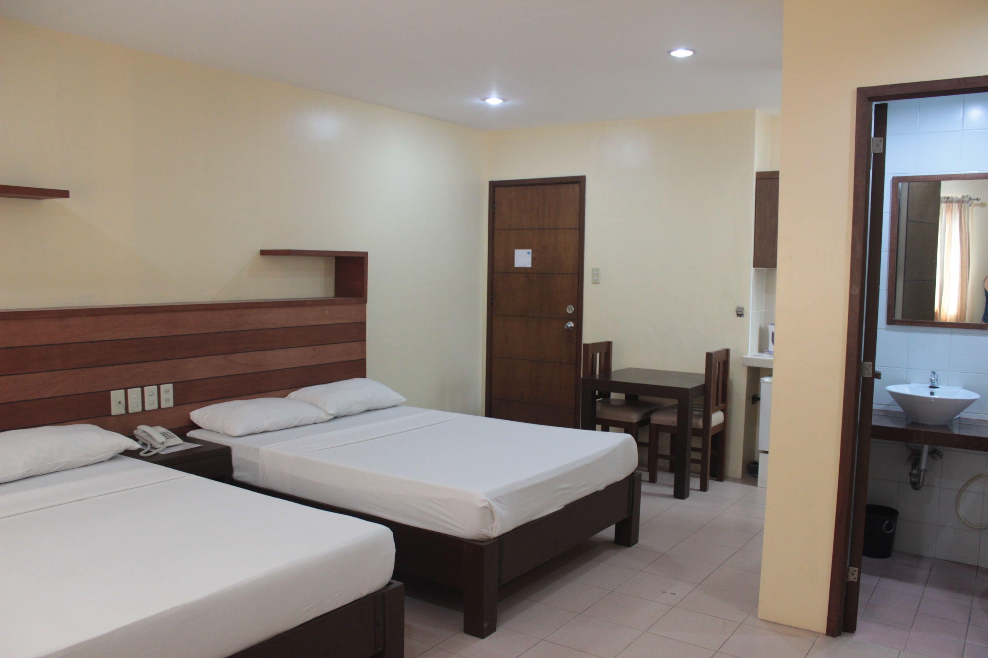 A hotel room with two beds, a desk, and a bathroom.