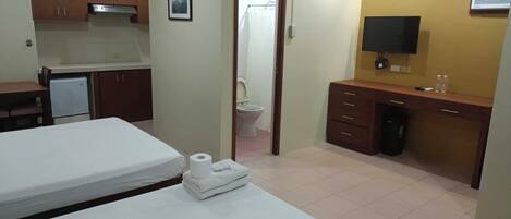 Una habitación de hotel con cama, una kitchenette pequeña, baño y televisor.
