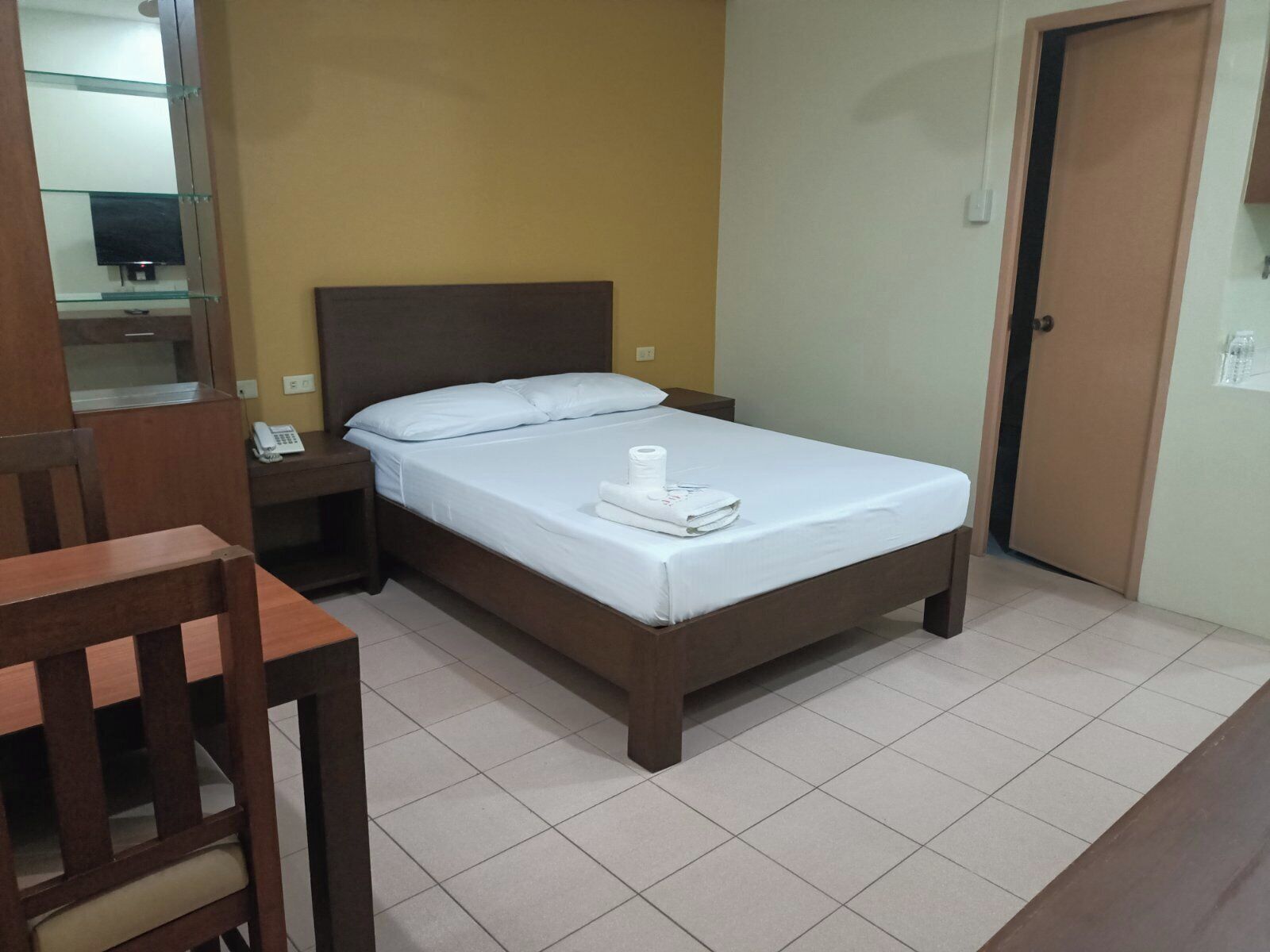 A single bed with a wooden headboard, a bedside table with a phone, and a chair.