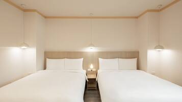 A hotel room with two single beds, a wooden headboard, a nightstand with a lamp, and pendant lights.