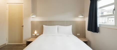 Una habitación de hotel ordenada con una cama grande, mesitas de noche y un ventanal con cortinas.