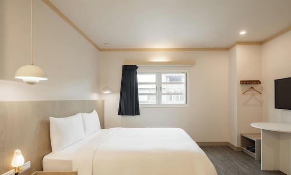 Hotellihuone, jossa on sänky, yöpöytä, lamppu, ikkuna ja seinälle asennettu televisio.