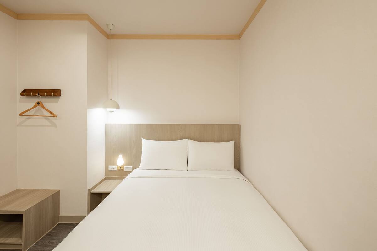 A neatly arranged hotel room with a bed, bedside table, and a hanging coat rack.