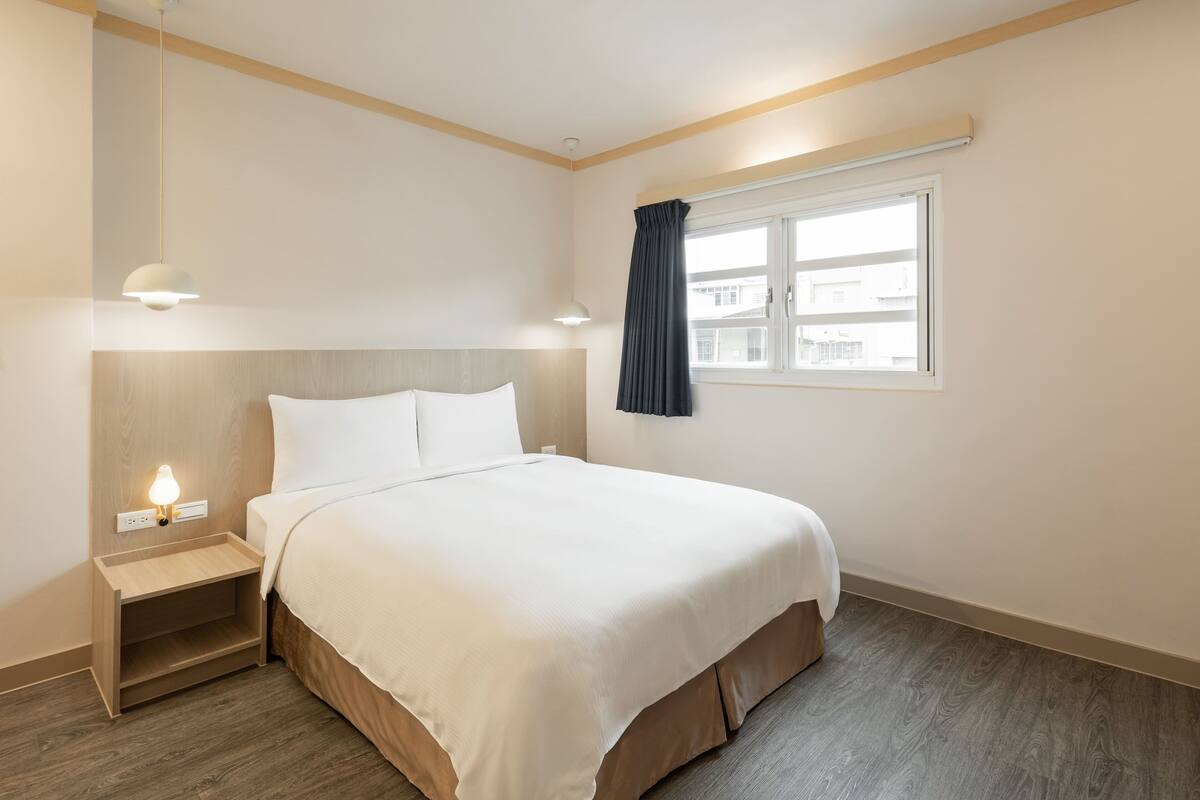 A neatly arranged hotel room with a bed, bedside table, lamp, and window.