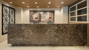 A reception desk with two staff members, a marble counter, and a geometric wall design. - Kindness Hotel Min Sheng (Tainan)