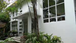 Un edificio moderno de dos pisos con ventanas amplias, un balcón y un jardín cuidado con diversas plantas.