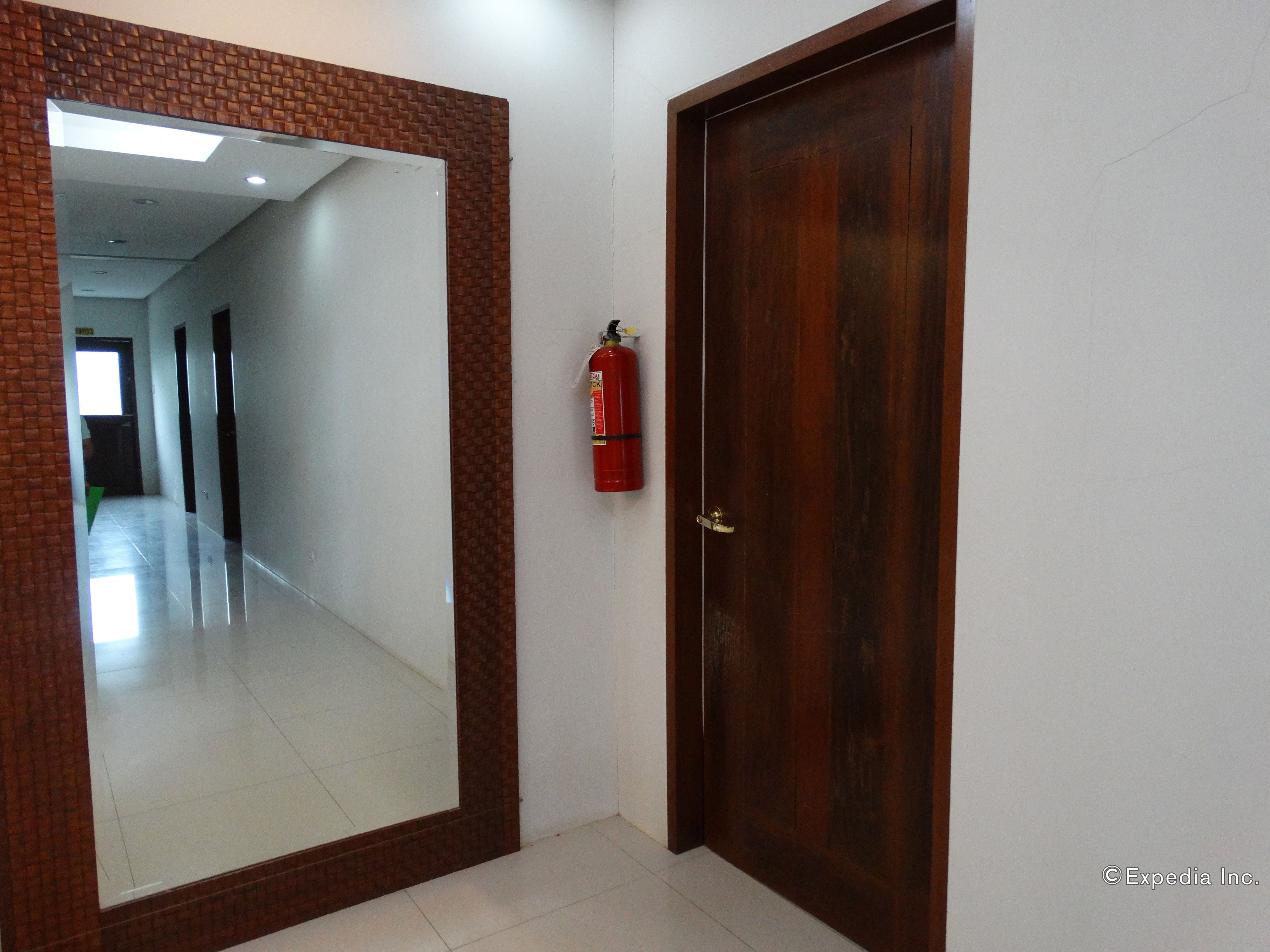 A hallway with a large mirror, a wooden door, and a fire extinguisher mounted on the wall.