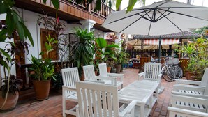 Un patio con sillas y mesas blancas, rodeado de plantas en macetas y una bicicleta.