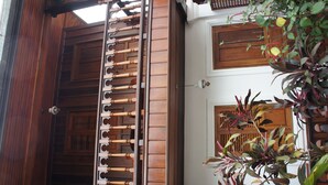 Una escalera de madera con barandilla, una pared blanca con una ventana y una planta de hojas rojas.
