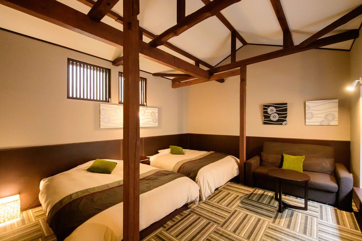 A hotel room with three beds, a sofa, a small table, and a patterned carpet.