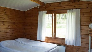 A single-bed room with wooden walls, a window with curtains, and a ceiling fan. - Wake Valley Camping (Ylojarvi)