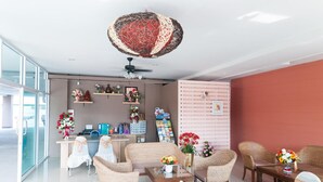 A modern hotel lobby with wicker furniture, a reception desk, and a large decorative ceiling light.