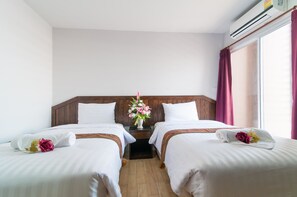Ett hotellrum med två sängar, en sänggavel i trä, ett nattduksbord med en vas med blommor och ett fönster med gardiner.