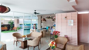 A modern hotel lobby with wicker furniture, a reception desk, and a view of the parking area.