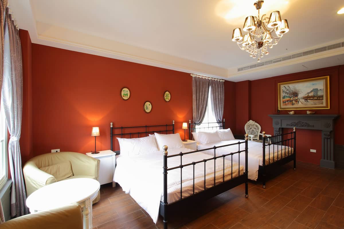 A bedroom with a four-poster bed, a bedside table with a lamp, a chair, and a fireplace.