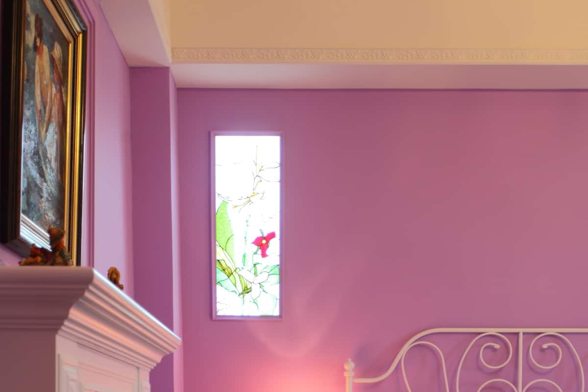 A bedroom with a bed, a nightstand, a lamp, and a window with a view of greenery.