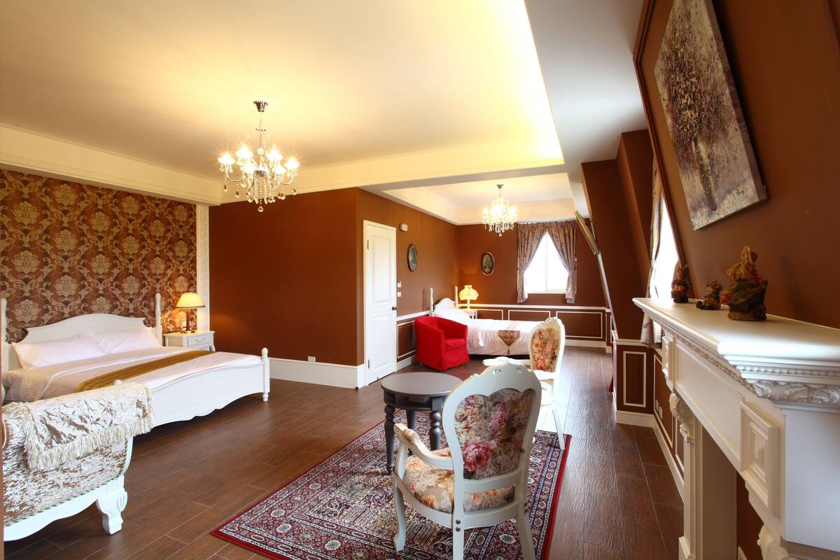 A room with a bed, a chair, a table, and a fireplace.