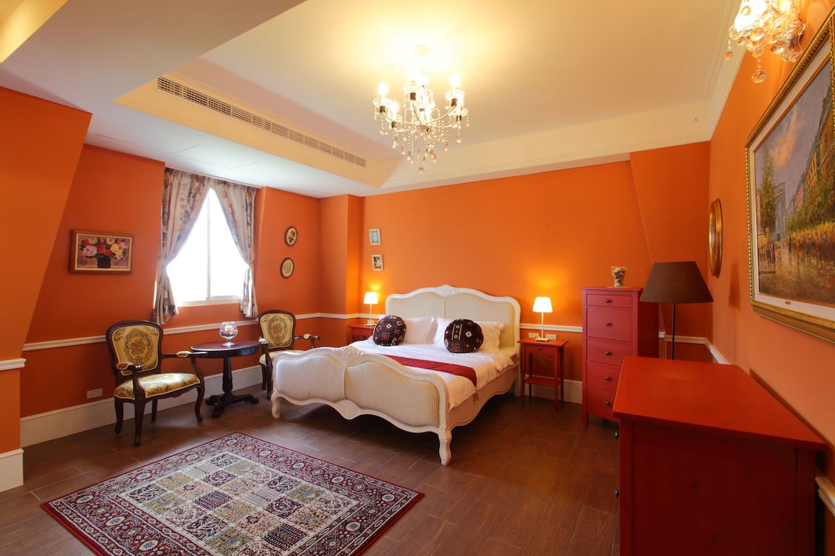 A bedroom with a large bed, a chandelier, a red dresser, and a patterned rug.
