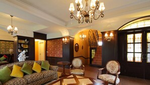 A spacious lobby with a patterned sofa, a round coffee table, and two armchairs. A chandelier hangs from the ceiling, and there are wall sconces and a large window with stained glass. - Haut-Rhin Villa (Zhuangwei)