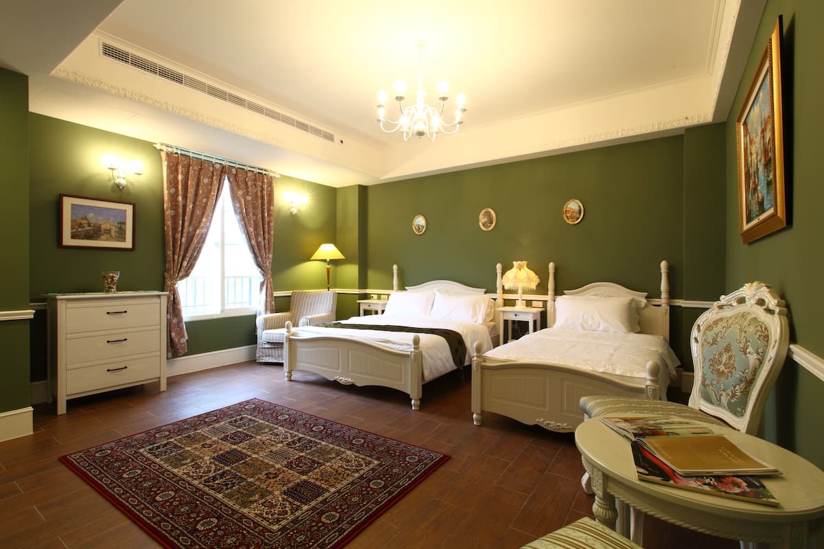 A bedroom with two beds, a chandelier, a large rug, and a painting on the wall.