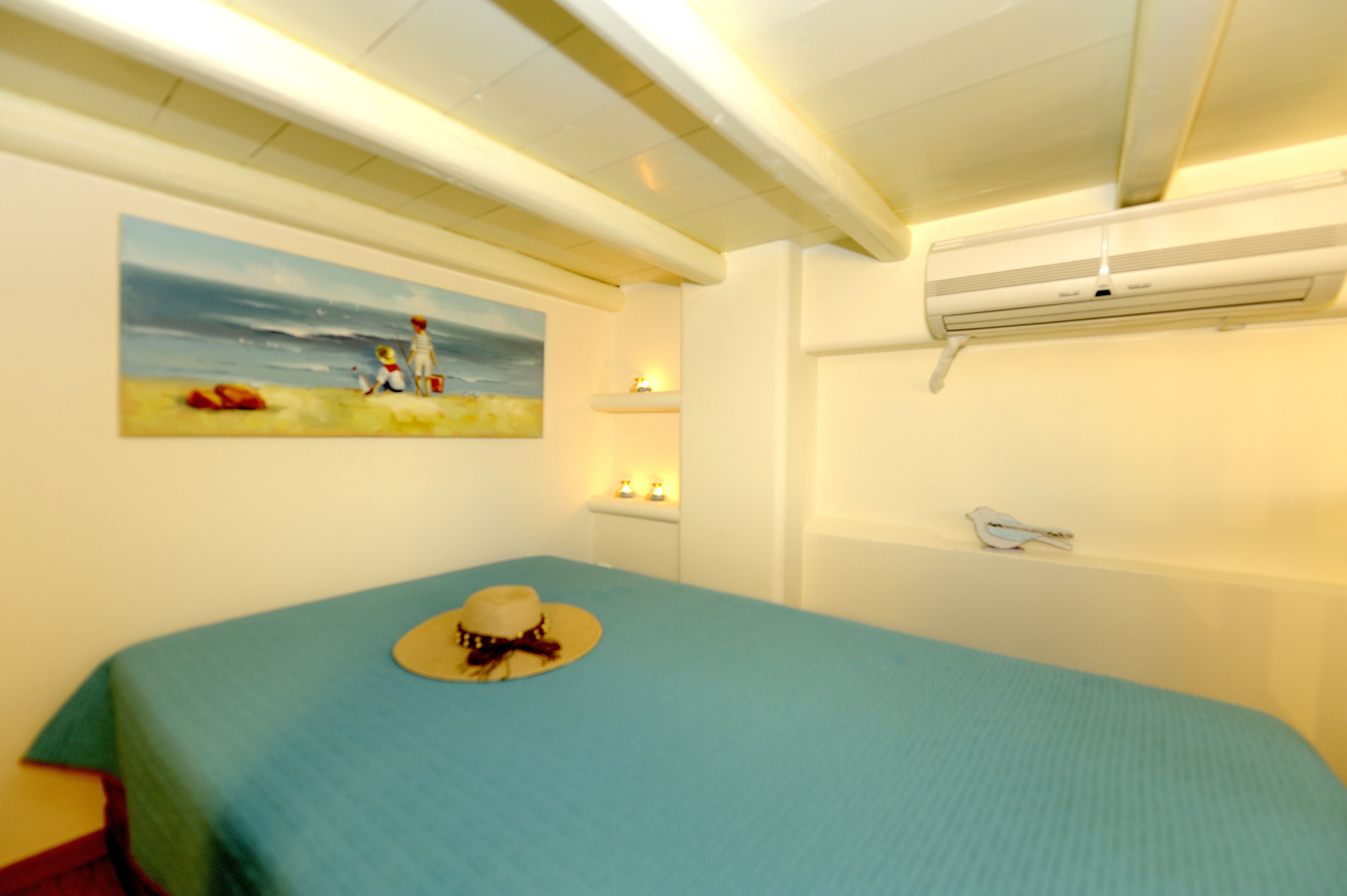 Een slaapkamer met een bed, een schilderij, een airconditioner en een nachtkastje met een lamp.