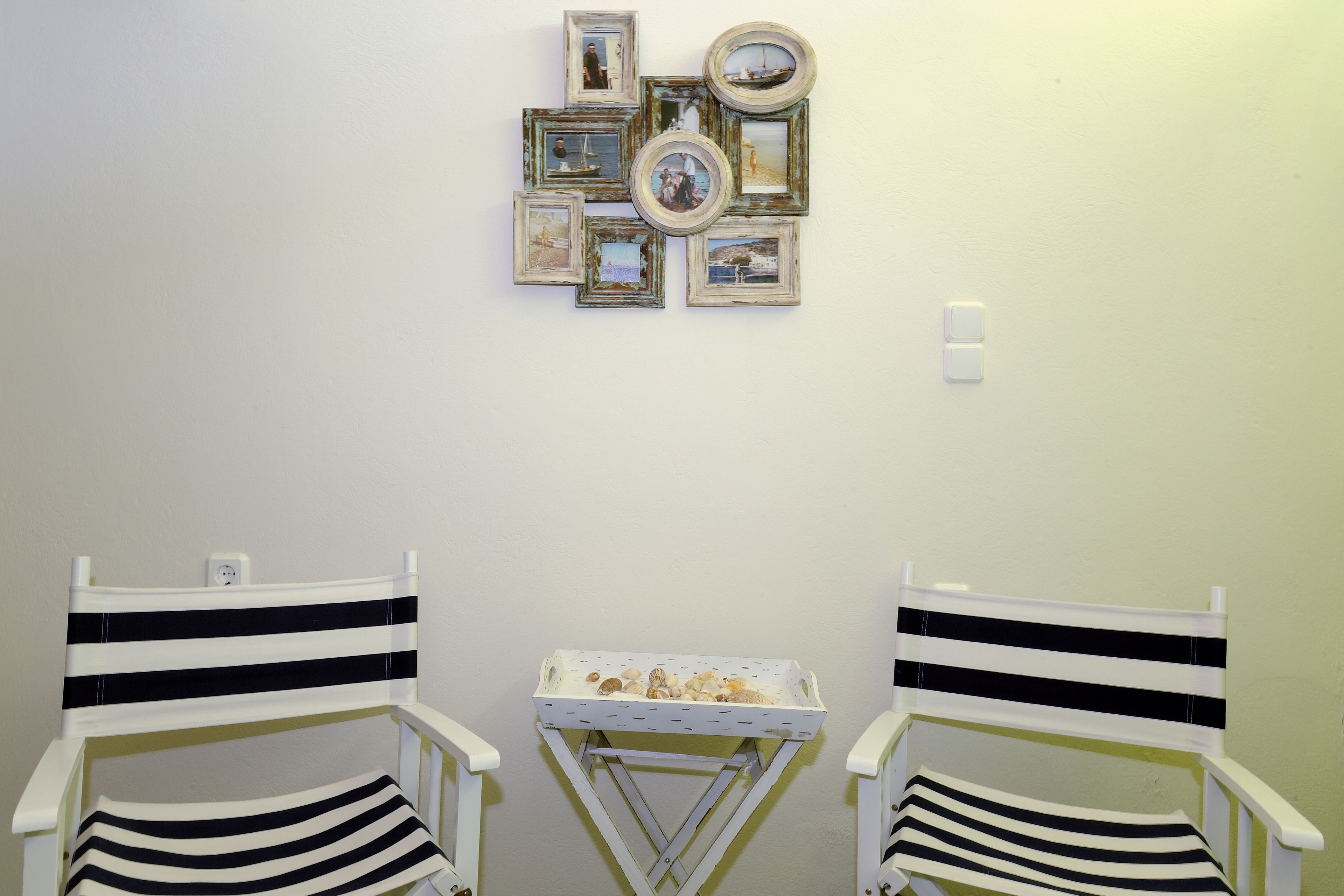 Two white chairs with black stripes, a small table with seashells, and a wall decorated with framed pictures.