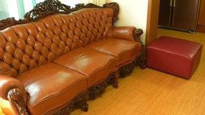 A brown leather sofa with a high back and ornate carvings, positioned next to a wooden floor and a red ottoman. - Kame House - Hostel (Seoul)