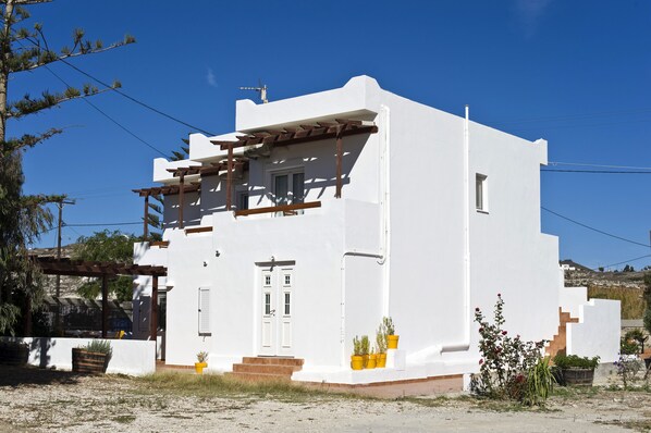 Un edificio blanco con una pérgola de madera, una puerta y escalones que conducen a un porche.