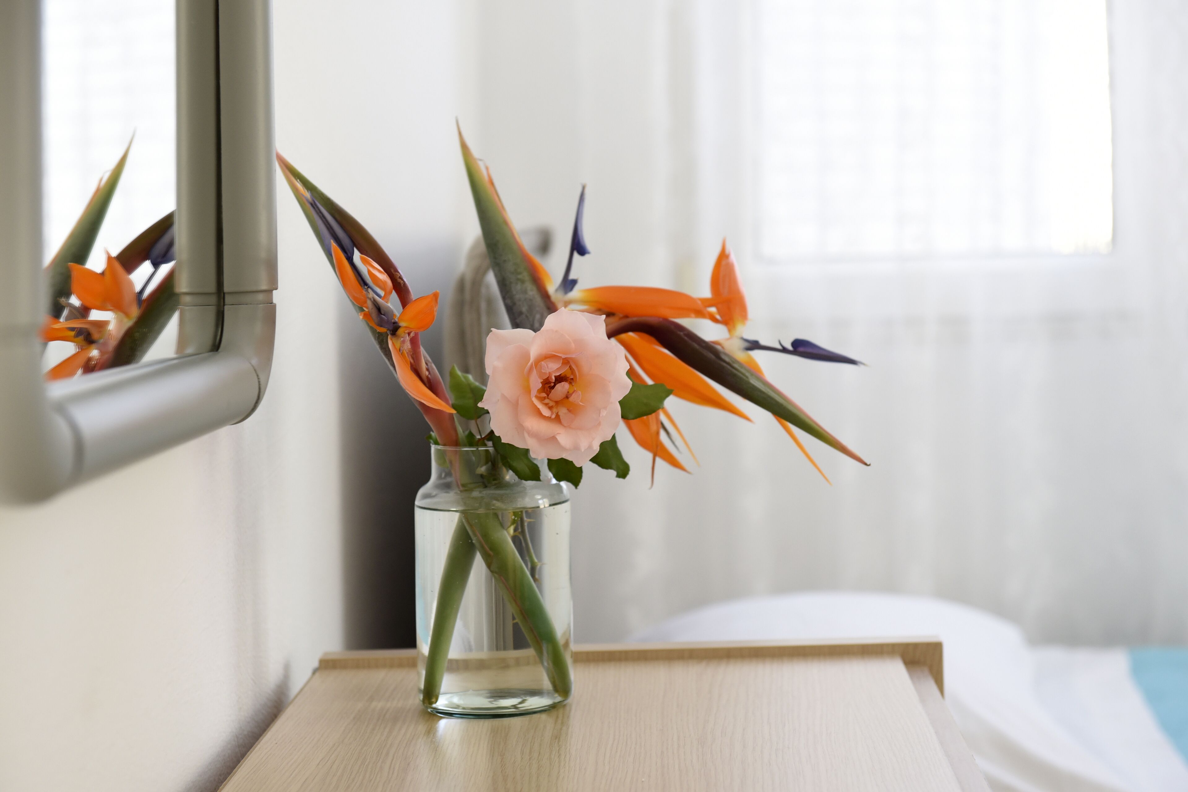 Vista clara de un baño con tocador de madera, un espejo y un florero con flores en la encimera.