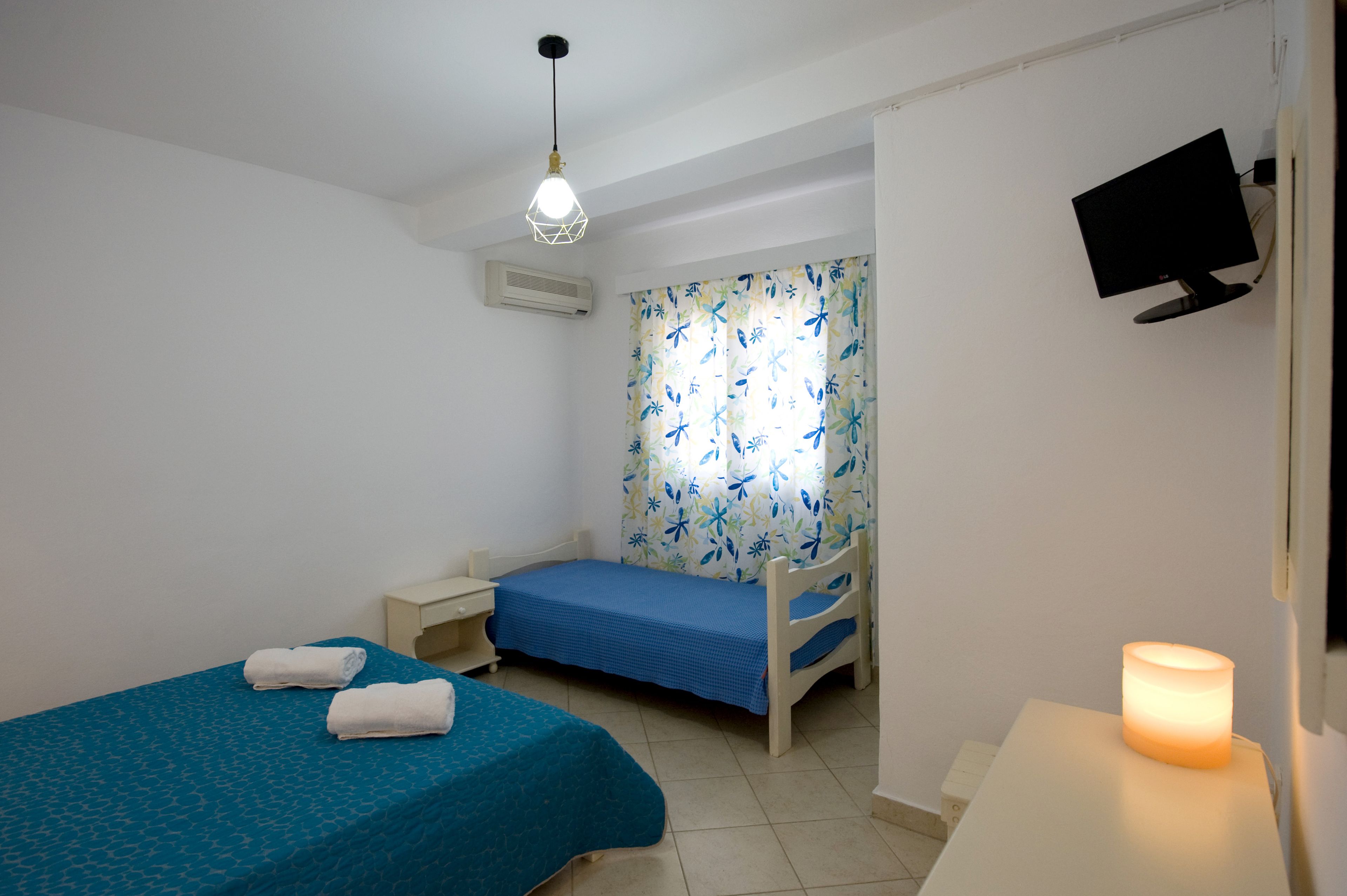 A small, clean room with two beds, a desk, a TV, and a lit candle.
