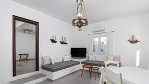 A modern living room with a large mirror, a chandelier, a flat-screen TV, and a dining area with a table and chairs. - Tsakanos Home (Milos)