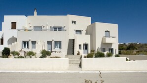 A modern white building with a staircase leading to the entrance, surrounded by small plants and a clear blue sky. - Tsakanos Home (Milos)