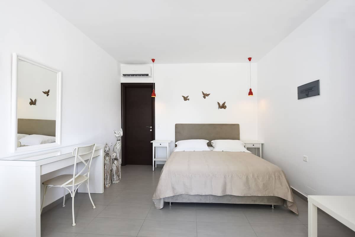 A bedroom with a bed, a desk, a chair, and a mirror.