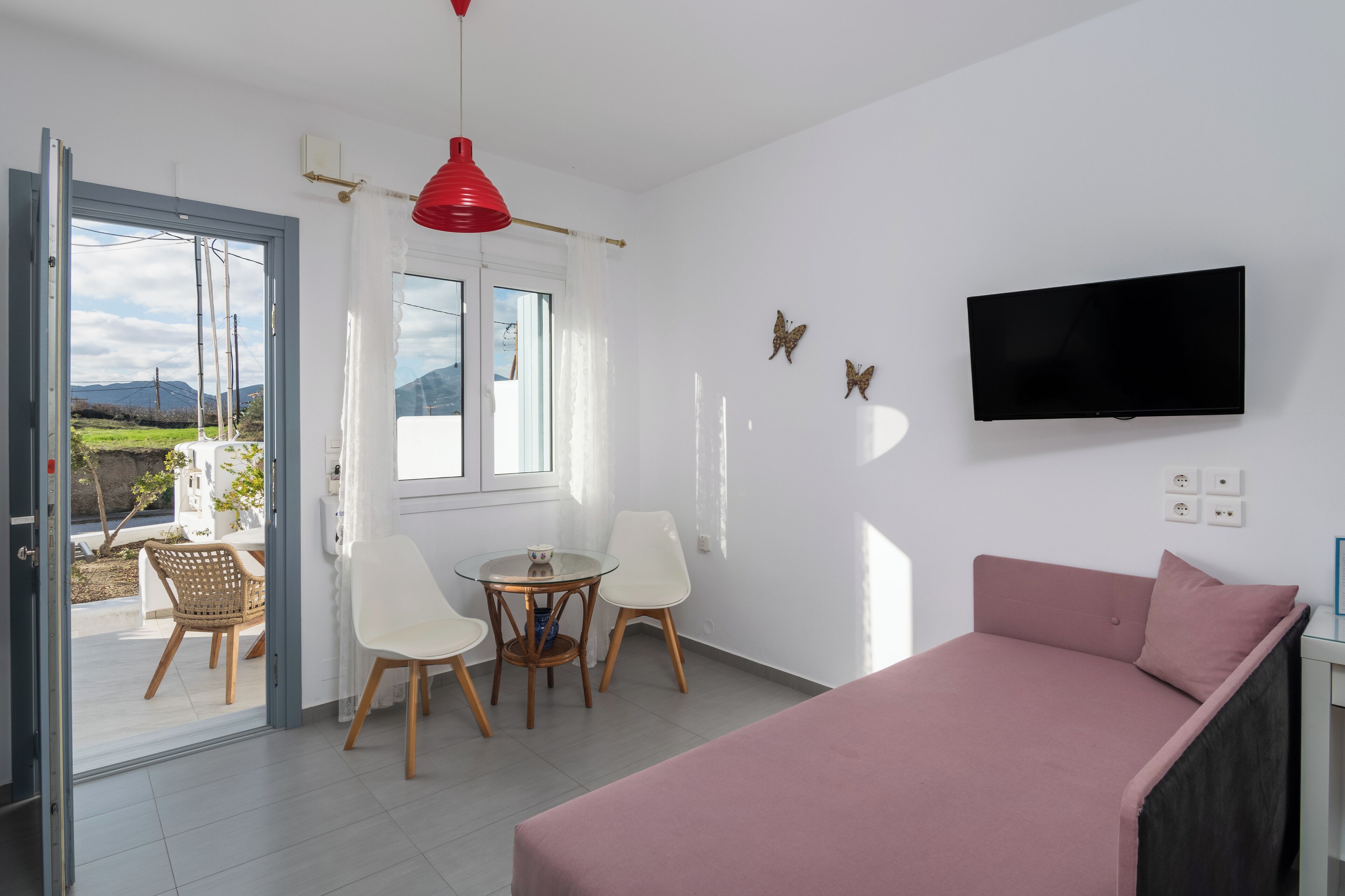 Una habitación moderna con cama, televisor, zona de comedor con sillas y vistas al exterior.