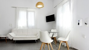 A modern living room with a white sofa, two white chairs, a small table, and a TV mounted on the wall. - Tsakanos Home (Milos)