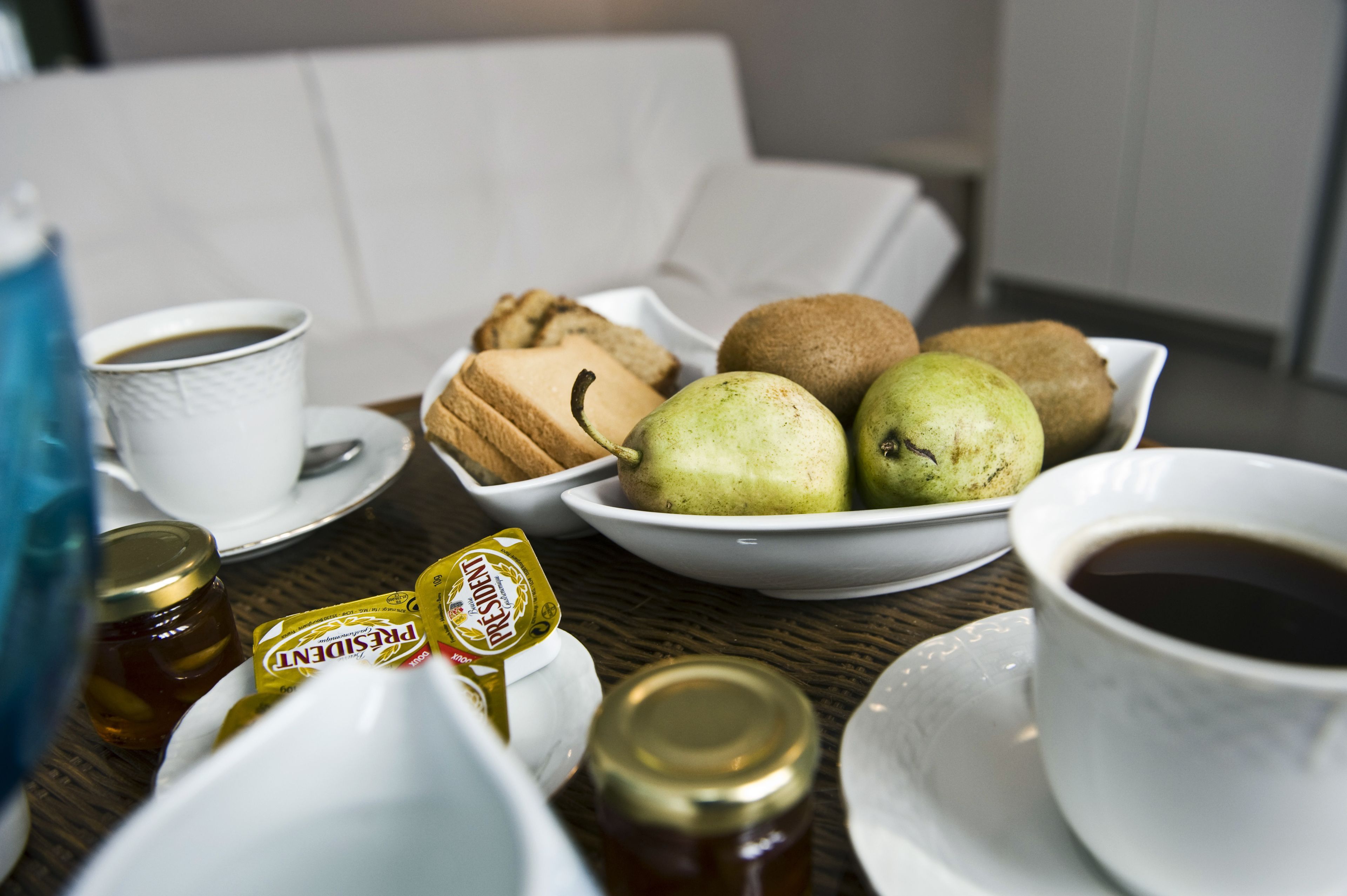 A table with a white cup of coffee, a bowl of pears, a plate of cookies, and jars of honey.