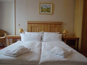 A neatly made bed with white linens, two bedside tables with lamps, and a framed picture on the wall. - Strandhotel Möwe (Heringsdorf)