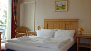 Habitació d'hotel amb un llit, una cadira, una tauleta de nit i una finestra amb cortines.
