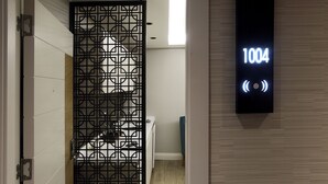 Une chambre d’hôtel au design moderne, avec une porte ornée d’un motif géométrique et un écran numérique affichant le numéro de chambre : 1004.