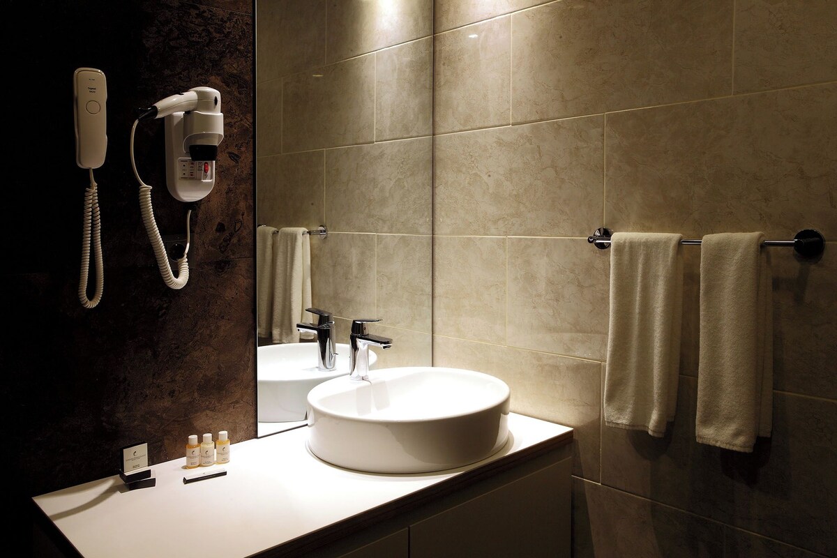 Een badkamer met een rond wastafel, een haardroger en een handdoekrek.