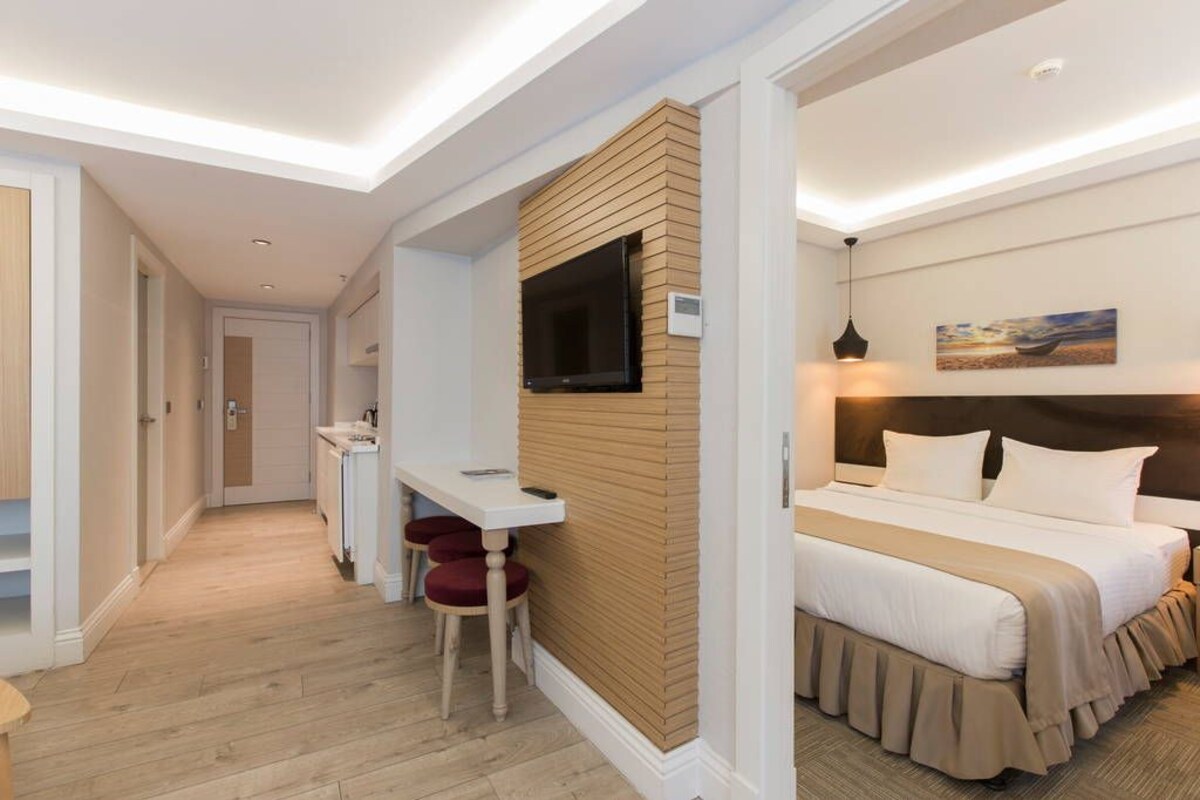 Ein Hotelzimmer mit einem Bett, einem Schreibtisch mit Stuhl, einem an einer Holzplatte montierten Fernseher und einem Bild an der Wand.