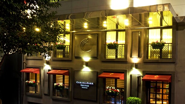 Un hôtel doté de plusieurs suites, chacune ayant un auvent rouge et une fenêtre ornée d’une plante. Le nom de l’hôtel est visible sur la façade.