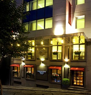 Ein Hotel mit mehreren Suiten, jede mit einem roten Markisenvorbau und einem Fenster mit einer Pflanze. Der Name des Hotels ist auf der Fassade sichtbar.