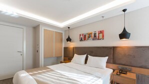 Une chambre d’hôtel moderne avec un grand lit, une tête de lit en bois, deux tables de chevet et une œuvre d’art accrochée au mur.