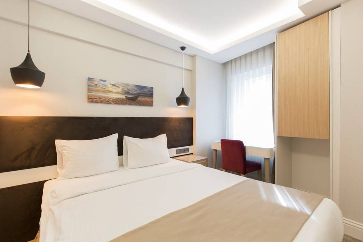 Een hotelkamer met een groot bed, twee hanglampen, een schilderij aan de muur, een bureau en een stoel.