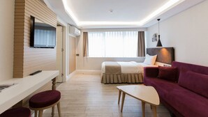 Une chambre d’hôtel moderne équipée d’un lit, d’un canapé, d’un bureau avec une chaise et d’un téléviseur fixé au mur.
