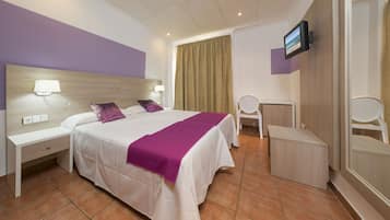 Habitación de hotel con cama, mesitas de noche, escritorio, silla, televisor y baño con espejo.