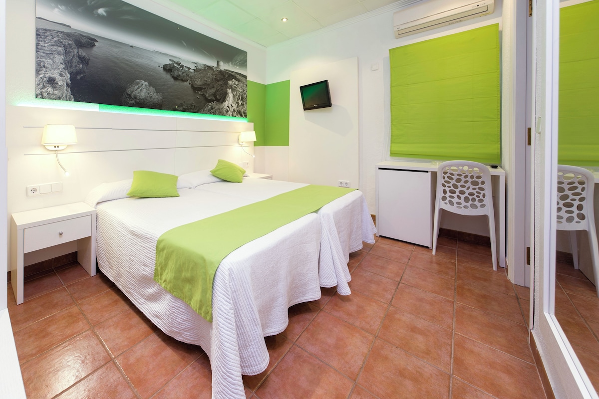 Une chambre d’hôtel avec un lit, un bureau, une chaise, une télévision et un mur vert.