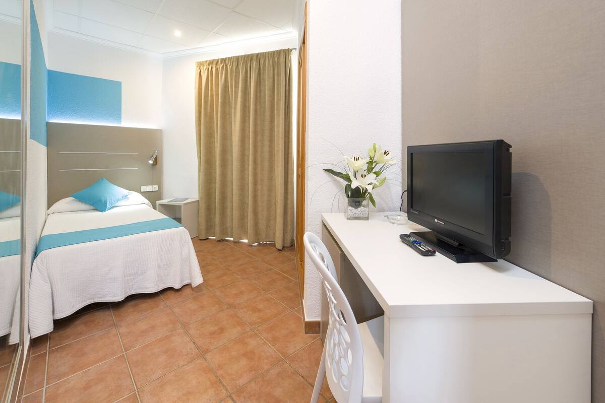 Ein Hotelzimmer mit Bett, Schreibtisch, Fernseher, Stuhl und einem Fenster mit Vorhängen.
