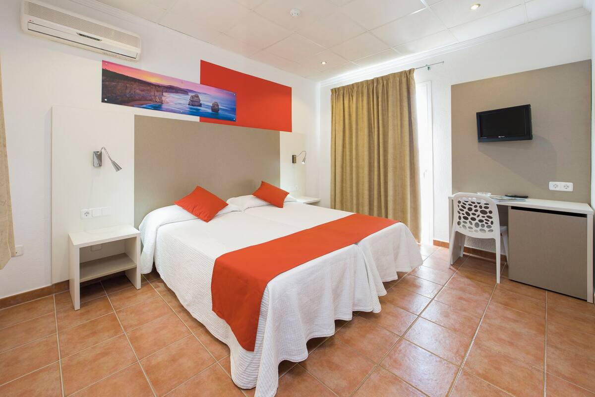 Ein Hotelzimmer mit Bett, Schreibtisch, Stuhl, Fernseher und einem Gemälde an der Wand.